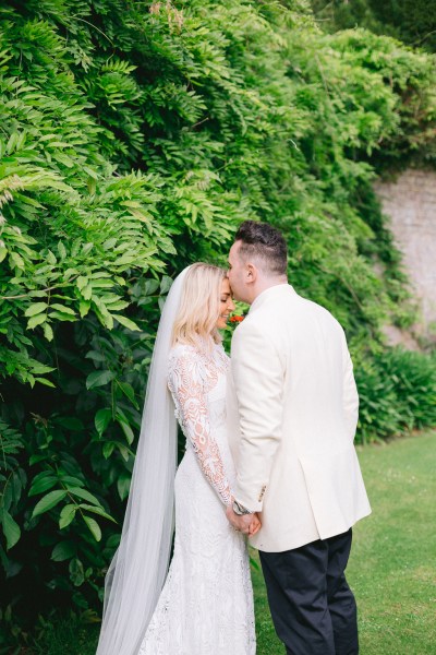 Bride and groom smiling in garden together kiss on the forehead