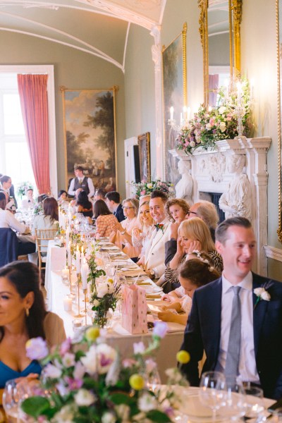 Bride and groom sit at the wedding table surrounded by guests