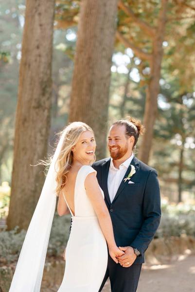 Bride and groom stand in forest holding hands