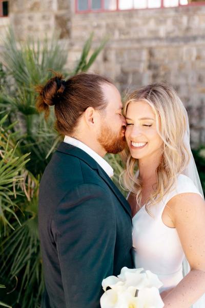 Groom kisses bride on the cheek as she smiles