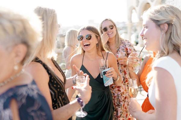 Guests wearing sunglasses holding beverages laughing and chatting