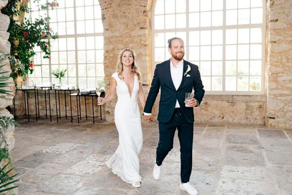 Bride and groom holding glass of champagne and beverage walk into ballroom