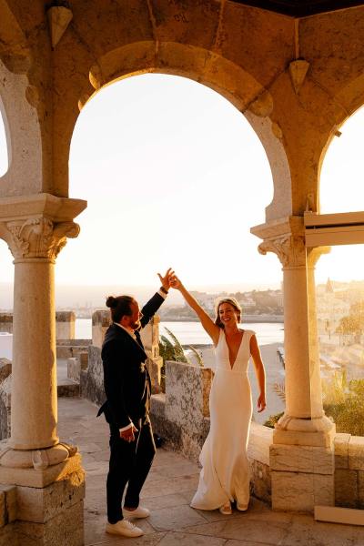 Bride and groom holding hands in the air sunset pillars on either side of them