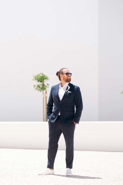 Groom on his own stands in the sunshine wearing sunglasses