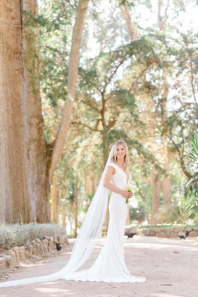 Bride stands on her own holding flowers in park forest setting