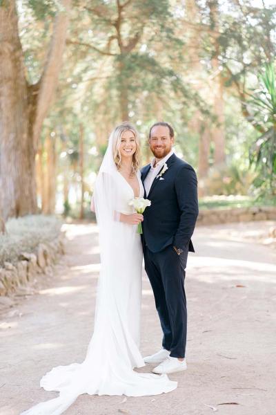 Bride and groom stand holding each other on pathway in park forest setting