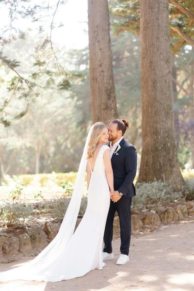 Groom kisses brides cheek veil dress detail from behind forest park setting