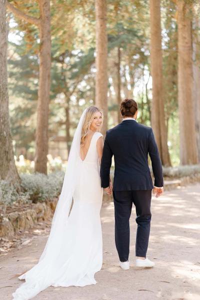 Bride and groom walking away from camera holding hands in forest park setting