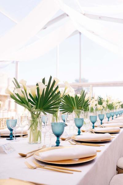 Blue cups golden plates cutlery and flowers on dining room table marquee setting