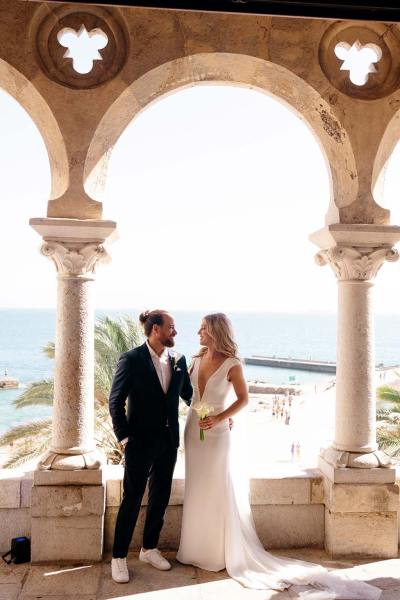 Bride and groom look at each other standing on balcony pillars behind them