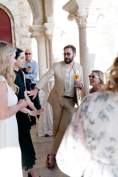 Groom standing beside pillar with bride and guests