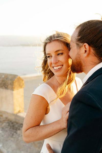 Bride smiling as she's being hugged by groom on balcony