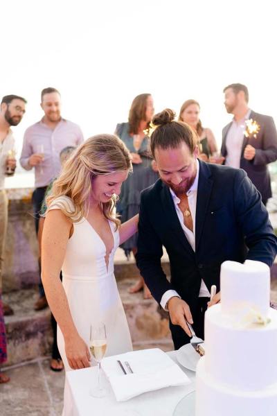 Bride and groom stand in front of pillars sunset in background twirl dancing on balcony