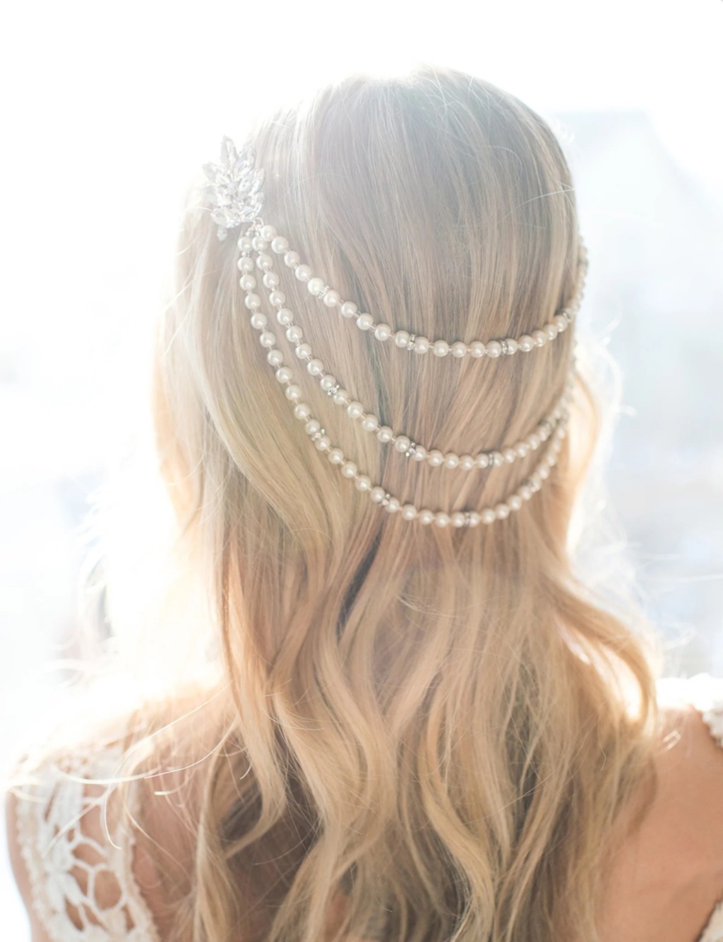 A model with blonde hair wears a pearl hair chain in her hair with a white lace wedding dress