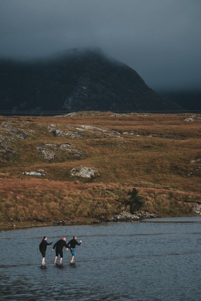 Groom and groomsmen walk in lake water gloomy rainy clouds in background