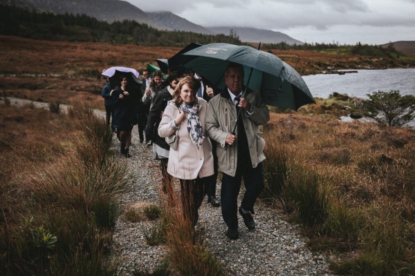 Trail of guests walking uphill on pathway holding black umbrellas