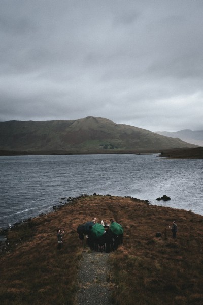 Guests walk downhill with green umbrellas sheltering from the rain drone shot mountain sea beach view