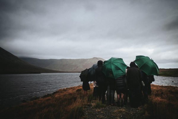 Guests walk downhill with green umbrellas sheltering from the rain