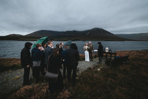 Evening windy dark shot of couple on edge of cliff umbrellas and guests