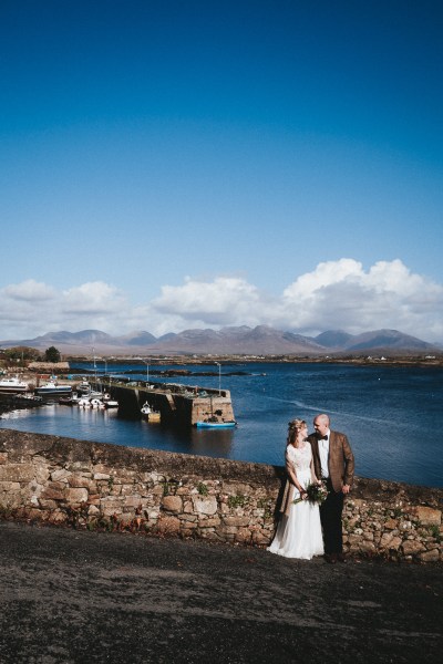 Bride and groom pose in front of rocky wall beach in background