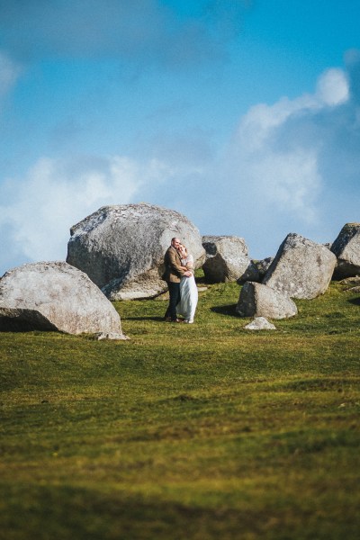 Bride and groom surrounded by rocks on grass mountain