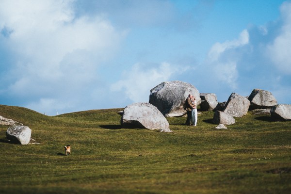 Bride and groom surrounded by rocks on grass mountain