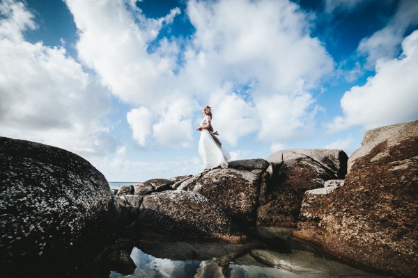 Bride with scarf blowing in the air skyline rocks beach in background