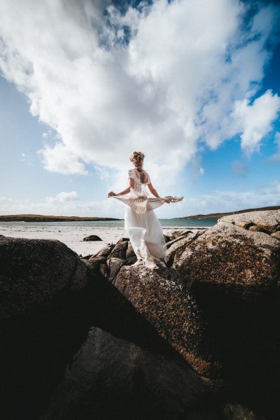 Bride with scarf blowing in the air skyline rocks beach in background