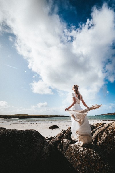 Bride with scarf blowing in the air skyline rocks beach in background