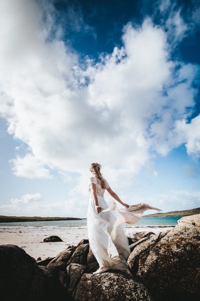 Bride with scarf blowing in the air skyline rocks beach in background