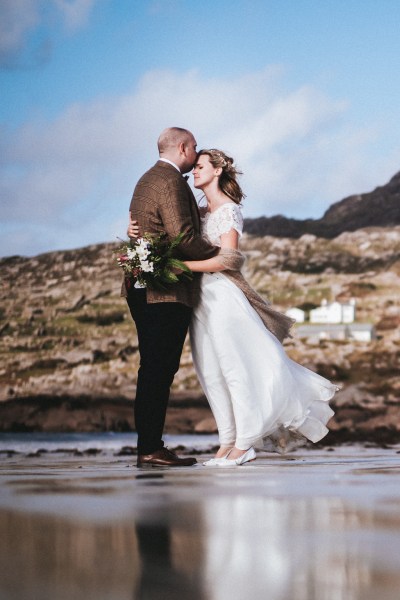 Bride and groom embrace on the beachy sand beach rocks mountains