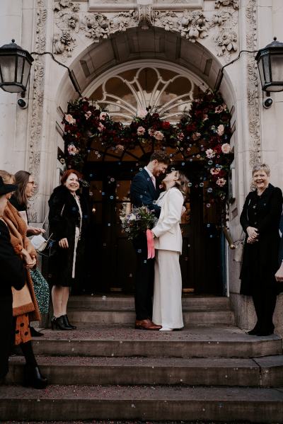 Bride and groom kiss outside church guests celebrate and cheer them on