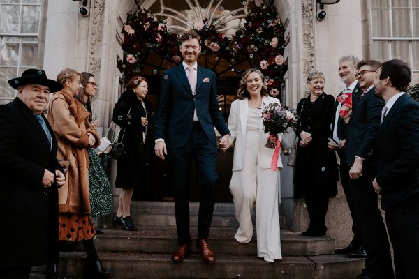 Bride and groom walk down the steps after ceremony ended guests clap and throw confetti on couple