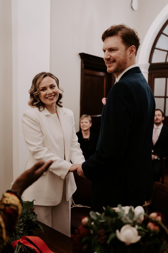 Bride and groom smile during ceremony holding hands