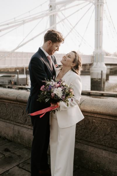 Bride and groom embrace hug along pathway bridge in background they smile and face each other