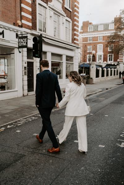 Bride and groom from behind walking hand in hand away from camera walking towards venue