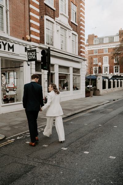 Bride and groom from behind walking hand in hand away from camera walking towards venue