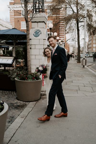 Bride and groom walking holding hands they look at camera