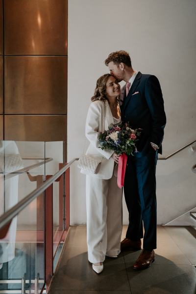 Bride and groom at top of stairs he kisses her on the head