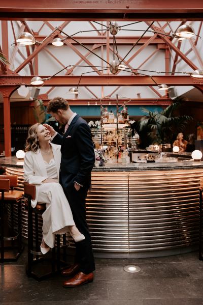 Bride and groom sit on stool groom looks at his bride and she looks at him