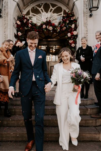 Bride and groom walk down the steps after ceremony ended guests clap and throw confetti on couple