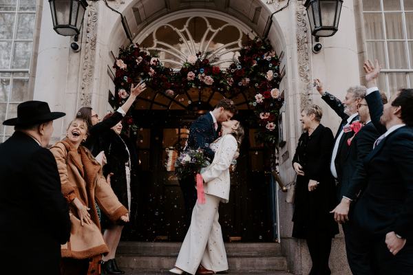 Bride and groom kiss outside church guests celebrate and cheer them on