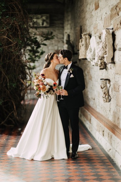 Bride and groom kiss on the red and black tiles as she holds bouquet