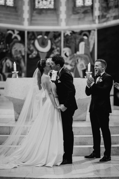 Groomsman claps as bride and groom kiss at alter