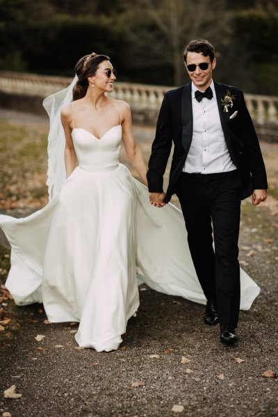 Bride and groom hand in hand holding hands along garden pathway