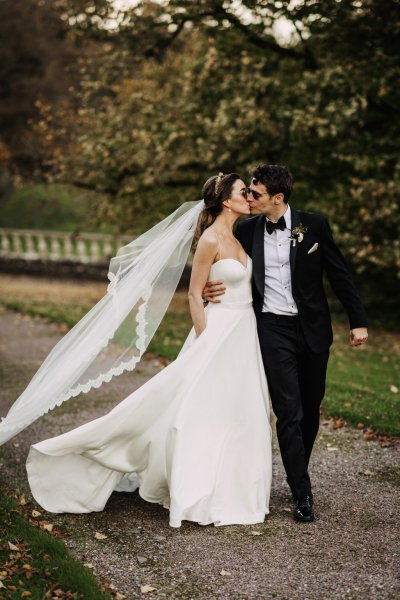 Bride and groom walk along pathway kissing