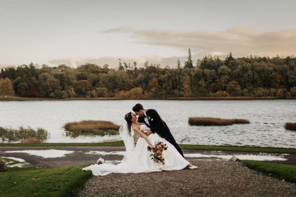 Groom leans in to kiss bride lake and trees in background