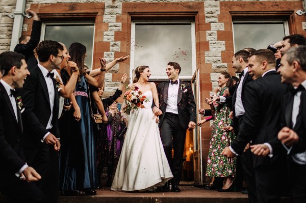 Bride and groom exit church surrounded by guests clapping and cheering