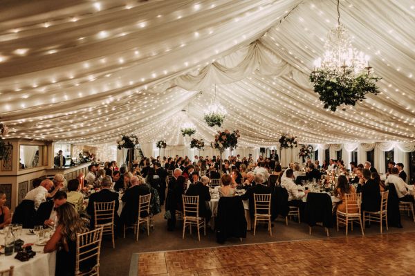 Guests seated at dining room tables under marquee tent