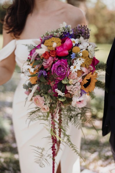 Bride poses on her own holding flowers bouquet containing colourful roses